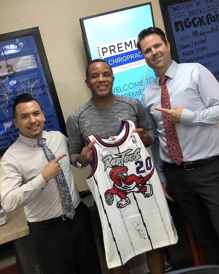 Former NBA Rookie of the Year Damon Stoudamire holds his signed Toronto Raptors number 20 jersey between Dr. Jesús Cazares and Dr. Christopher Schlenger at Premier Chiropractic