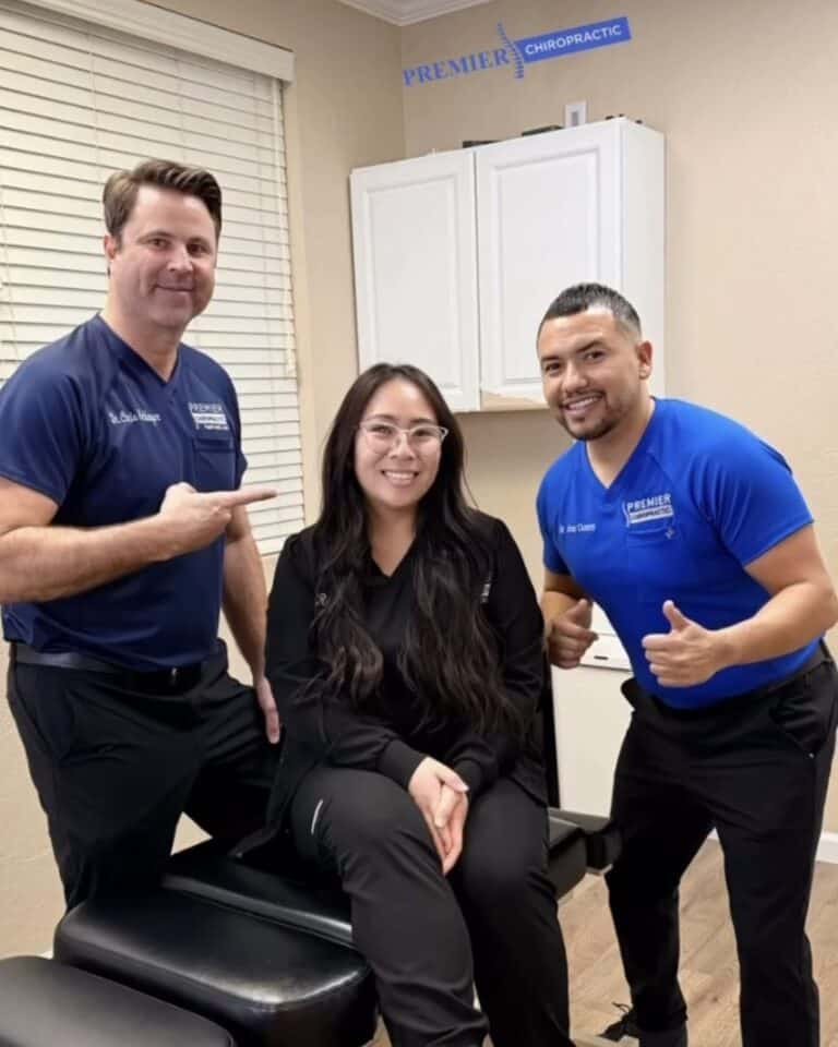 Dr. Christopher Schlenger and Dr. Jesús Cazares smile with a woman seated on an adjusting table at Premier Chiropractic